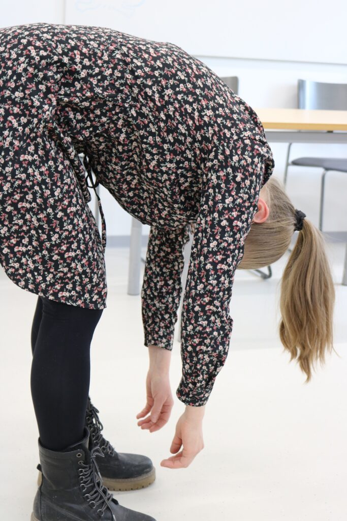 Henkilö kumartuu eteenpäin ja roikottaa käsiään kohti lattiaa.