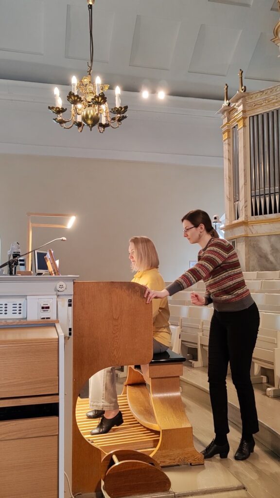 Henkilö soittaa urkuja ja opettaja seuraa vierestä.