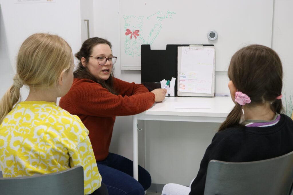 Kaksi lasta oppitunnilla opettajan ohjaamana.