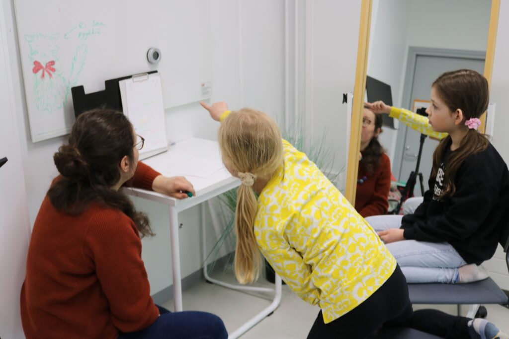 Opettaja ja kaksi oppilasta tunnilla, toinen oppilaista osoittaa taulua.