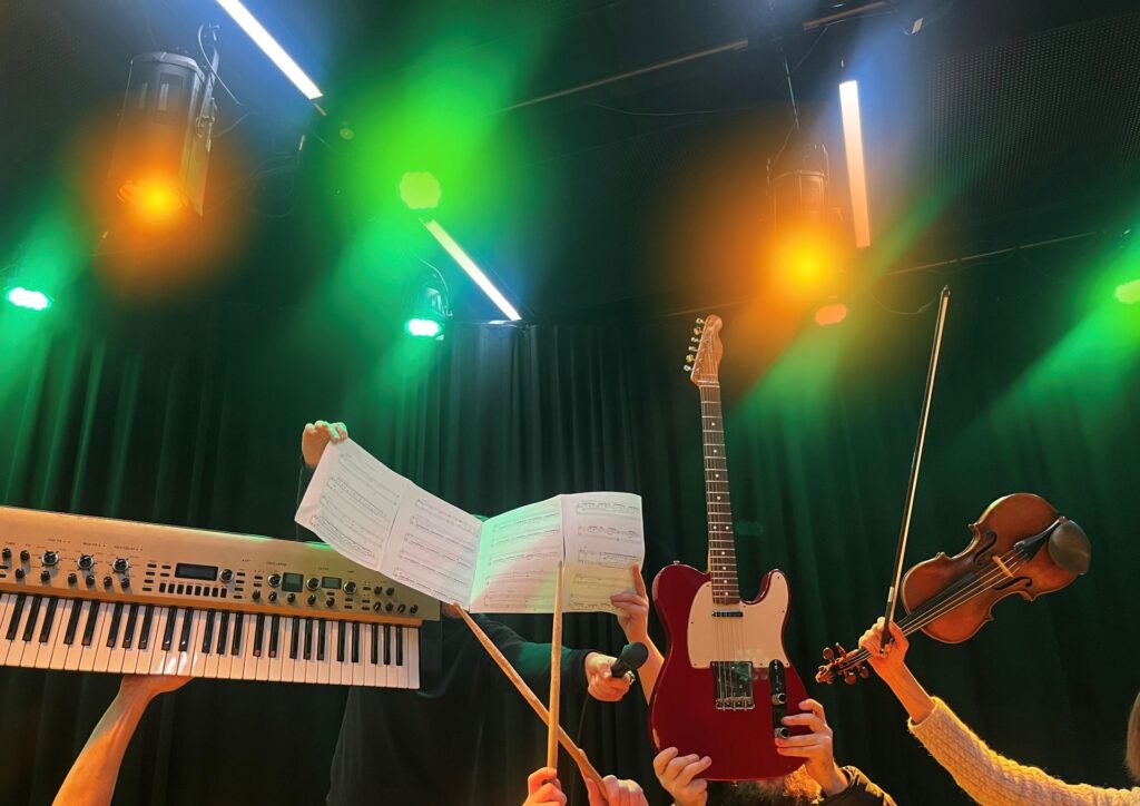 Musiikkikoulu Johtosävelen soittajia, jotka pitelevät ilmassa soittimia ja nuotteja.